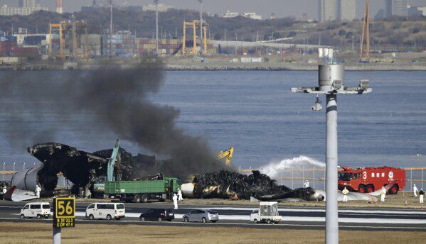 Black smoke rises as removal work is carried out at the site of an aircraft collision at Haneda Airport in Tokyo Friday, January 5, 2024. Cranes were dismantling Japan Airlines Flight 516 Airbus A350, which caught fire after colliding with a Coast Guard plane while they were dismantling the plane.  She was landing at the airport on Tuesday.  (Kyodo News via Associated Press)