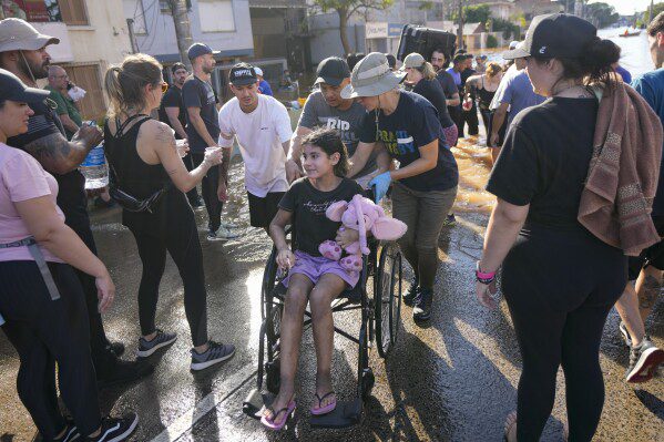 Volunteers push a wheelchair transporting an evacuee from an area flooded by heavy rain, in Porto Alegre, Brazil, Tuesday, May 7, 2024. (AP Photo/Andre Penner)