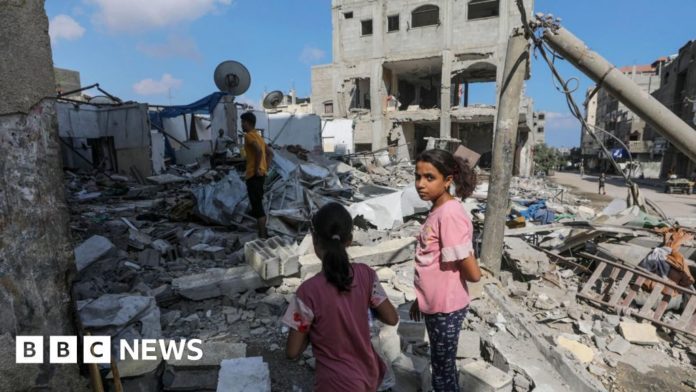 Two Palestinian girls and two men inspect a destroyed home in Magazi refugee camp, in the central Gaza Strip, following an Israeli air strike (14 August 2024)